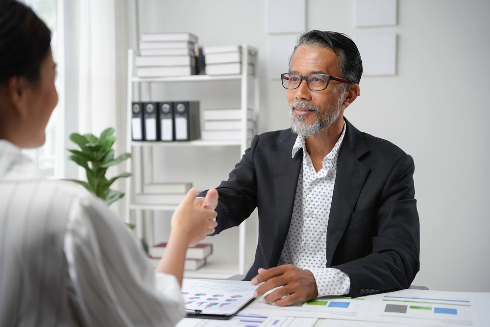 senior manager and young female professional shaking hands in a bright office during a business meeting