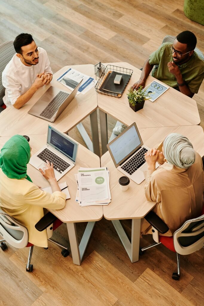 A diverse group of professionals engaged in discussion around a wooden table, focusing on laptops and documents.